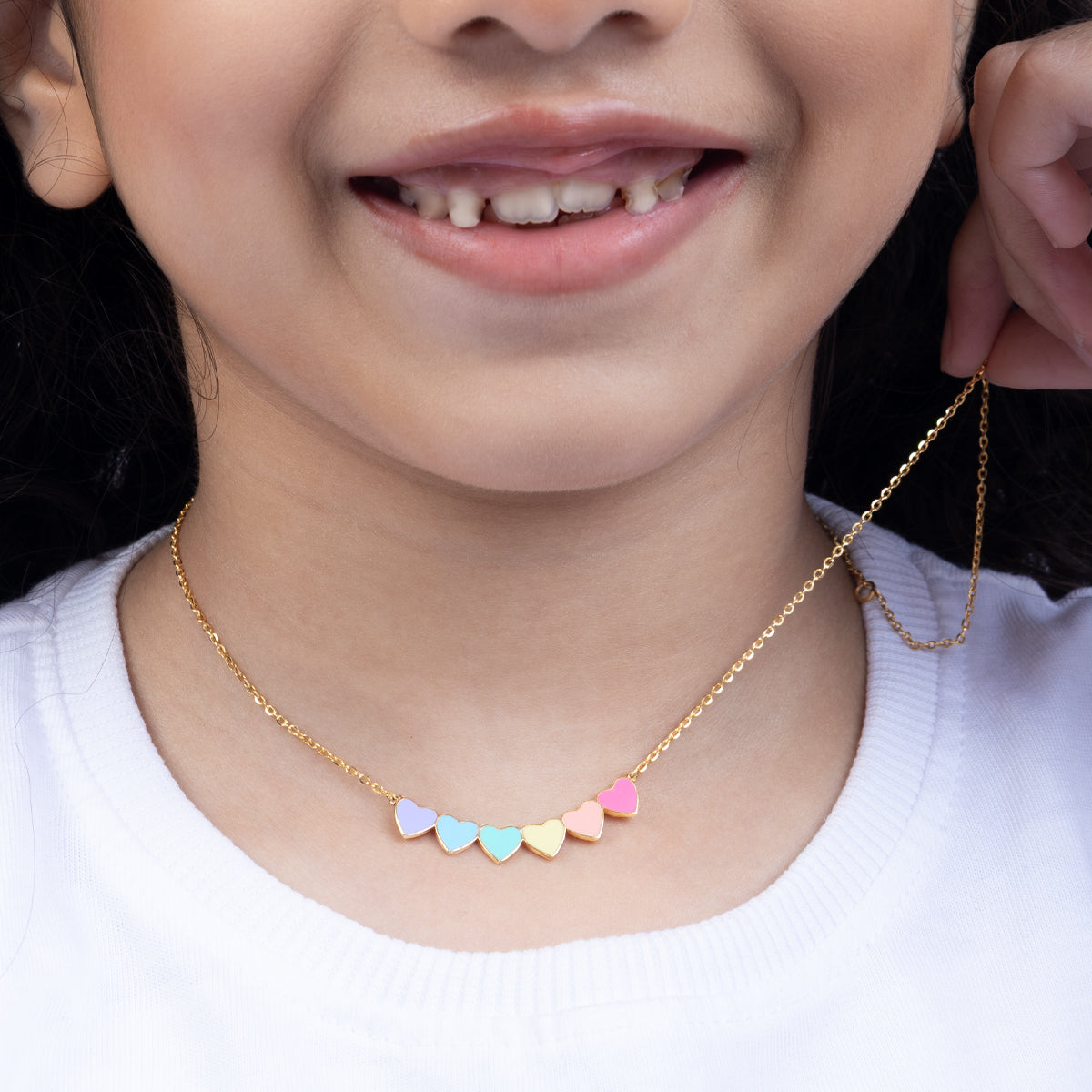 Tiny Jewels close-up of a child wearing a gold necklace with colorful heart-shaped pendants.