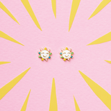 Tiny Jewels sun-shaped earrings on a pink background with yellow sunburst design