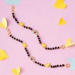 Tiny Jewels necklace with heart-shaped charms on a pink background with yellow heart shapes