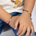 Tiny Jewels child's wrist wearing a black beaded bracelet with gold accents, sitting on a white surface.