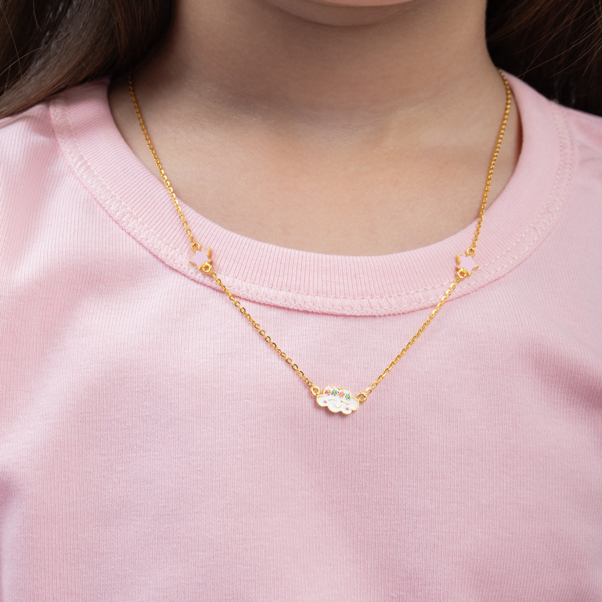 Tiny Jewels gold necklace with a small pendant worn by a person in a pink shirt