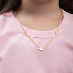 Tiny Jewels gold necklace with a small pendant worn by a person in a pink shirt