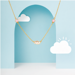 Tiny Jewels gold necklace with pink stars on a blue background with white clouds