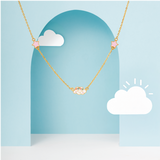 Tiny Jewels gold necklace with pink stars on a blue background with white clouds