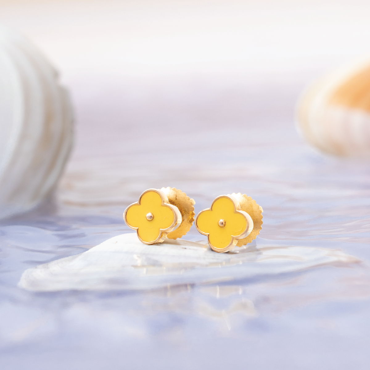 Tiny Jewels gold flower-shaped earrings on a white surface with a blurred background