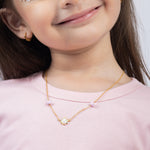 Tiny Jewels close-up of a child wearing a gold necklace with a pink background