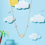 Tiny Jewels necklace with a bear pendant on a blue background with clouds and a palm tree