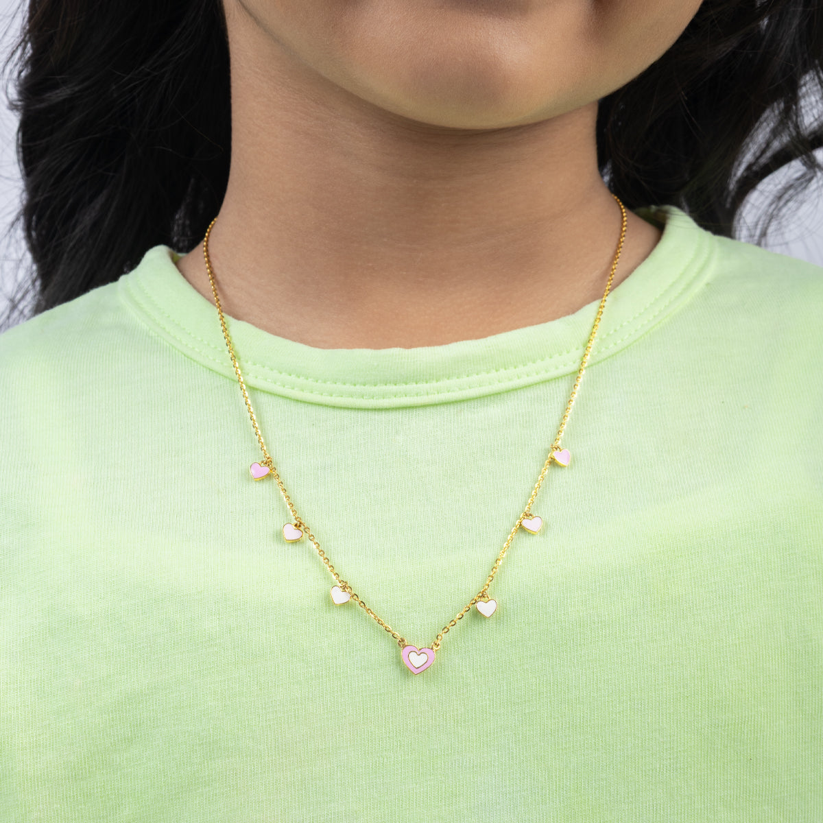 Tiny Jewels gold necklace with heart-shaped pendants worn by a person in a green shirt