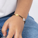 Tiny Jewels close-up of a child's hand wearing a bracelet with a blue and white flower charm, against a blurred background.