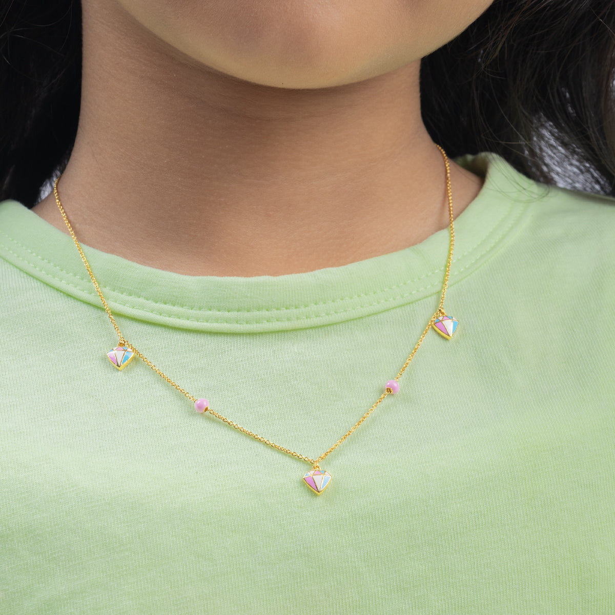 Tiny Jewels gold necklace with heart-shaped pendants worn by a person in a green shirt.
