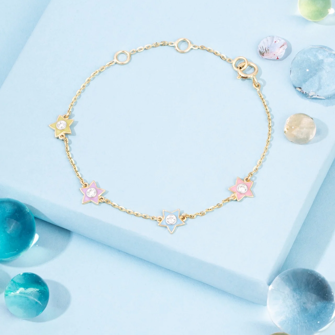Tiny Jewels gold bracelet with star-shaped charms on a light blue background