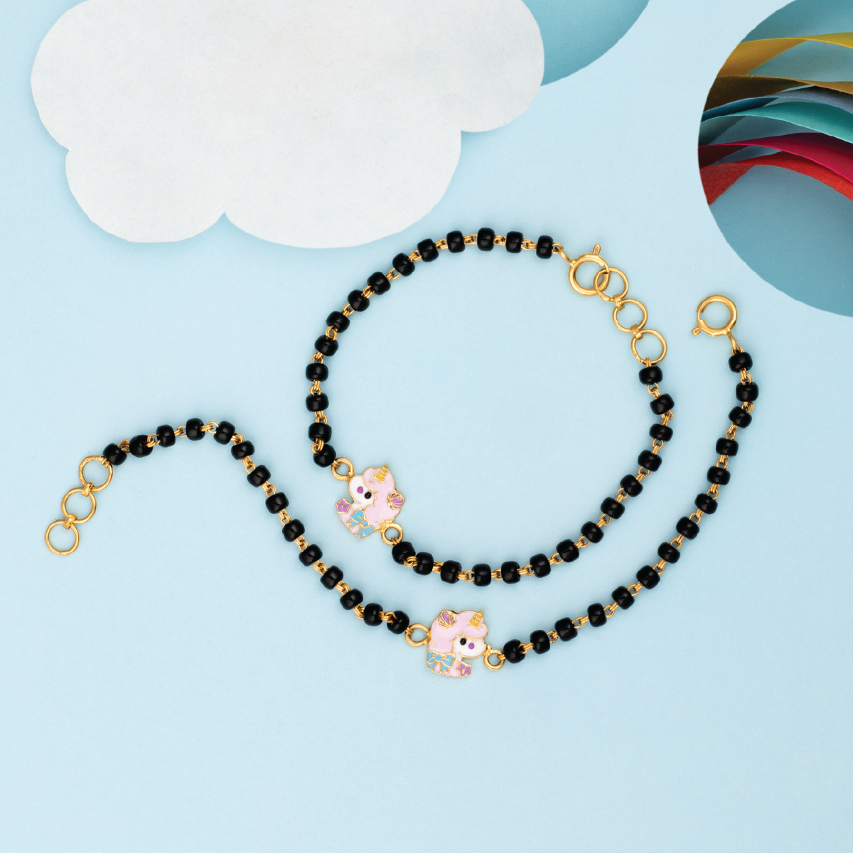 Tiny Jewels black beaded lanyard with gold accents and pink charms on a light blue background