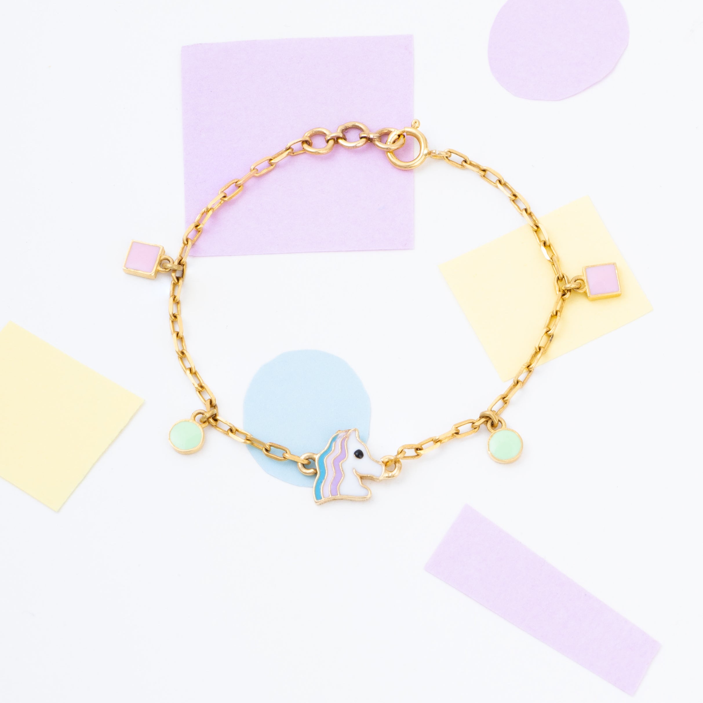 Tiny Jewels gold bracelet with a unicorn charm on a colorful background