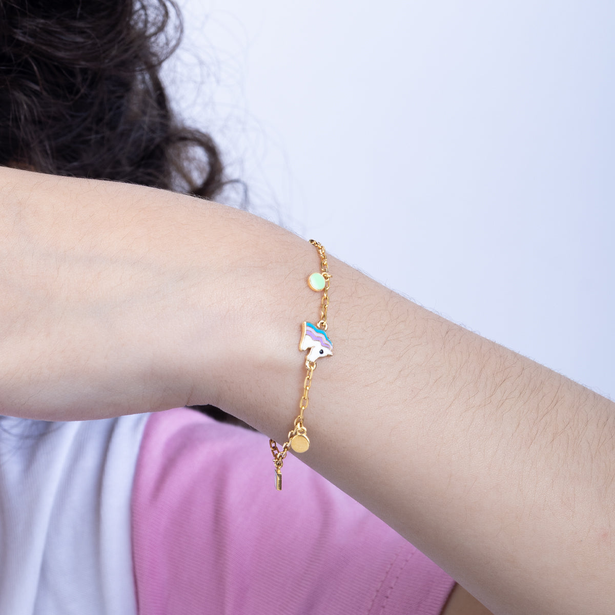 Tiny Jewels gold bracelet with charms on a person's wrist against a white background