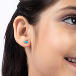 Tiny Jewels close-up of a person wearing a blue and gold earring.